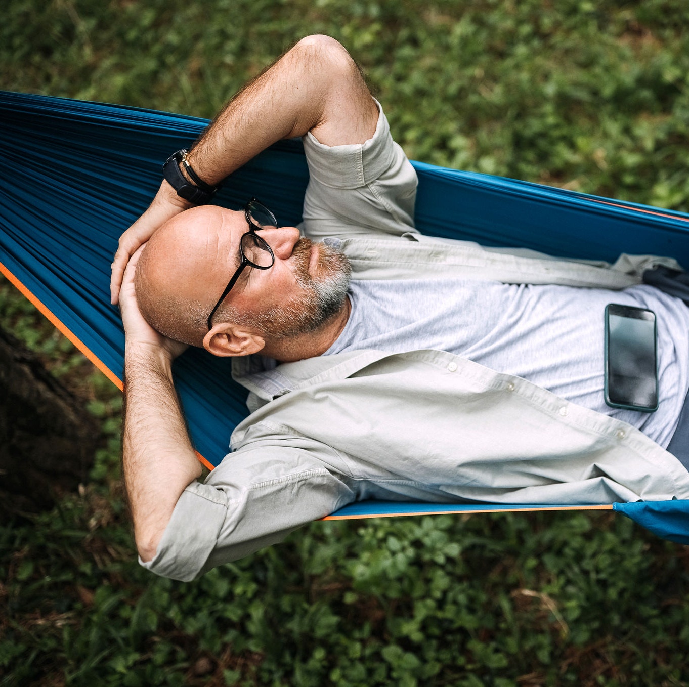 Senior man laying on hammock in nature and using smart phone