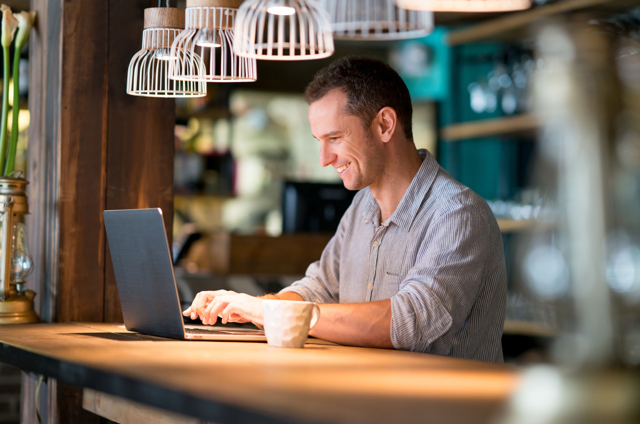 Smiling male working online at a cafe and drinking a cup of coffee