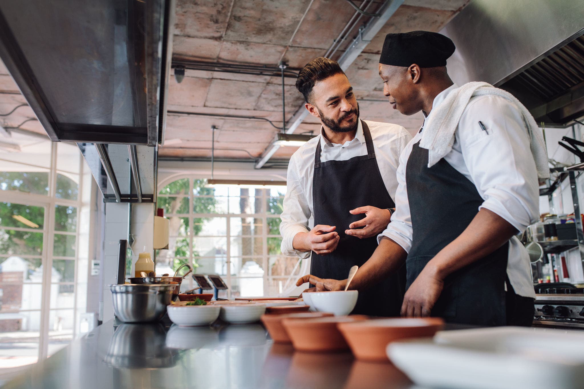 Chefs talking while cooking food in commercial kitchen Two male cooks preparing food on restaurant kitchen. Chefs talking while cooking food in commercial kitchen.