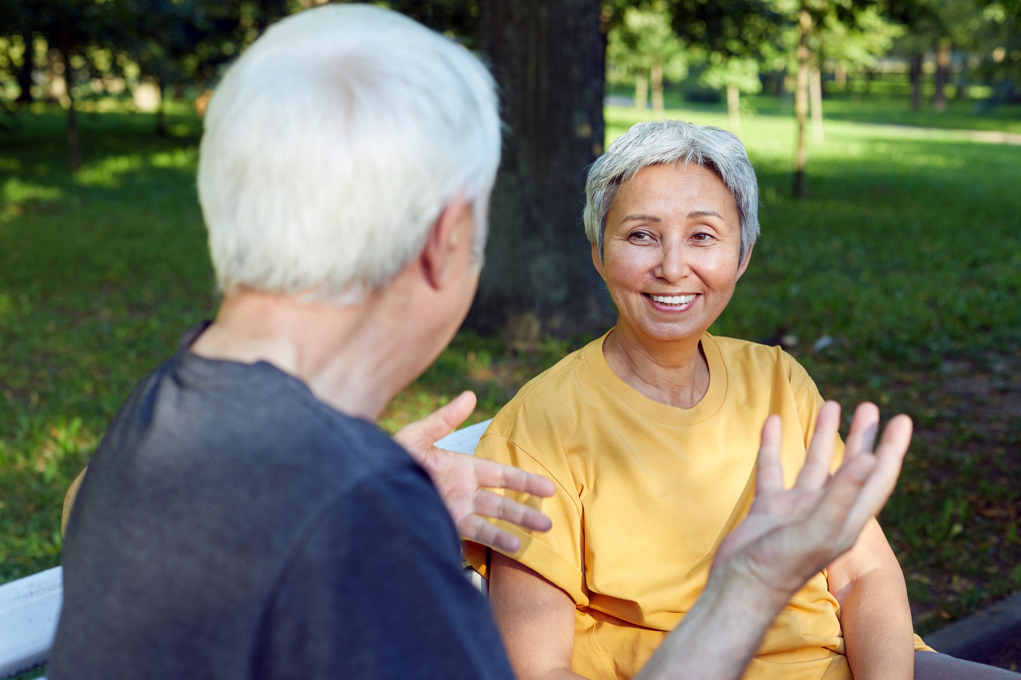 Middle-aged couple multi-ethnic spouses sit rest on bench enjoy talk in public summer park having friendly conversation share thoughts or news during meeting outdoors. Relations, marriage concept