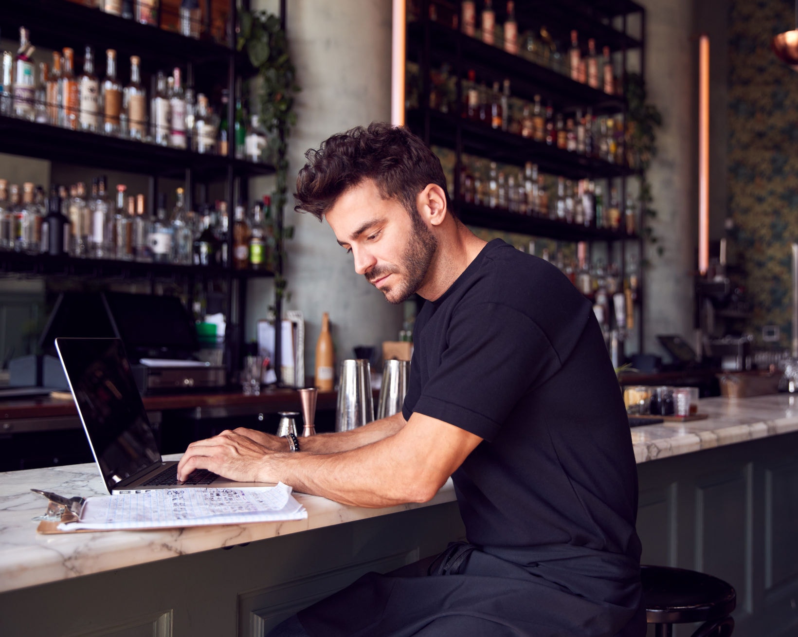 Male Owner Of Restaurant Bar Sitting At Counter Working On Laptop
