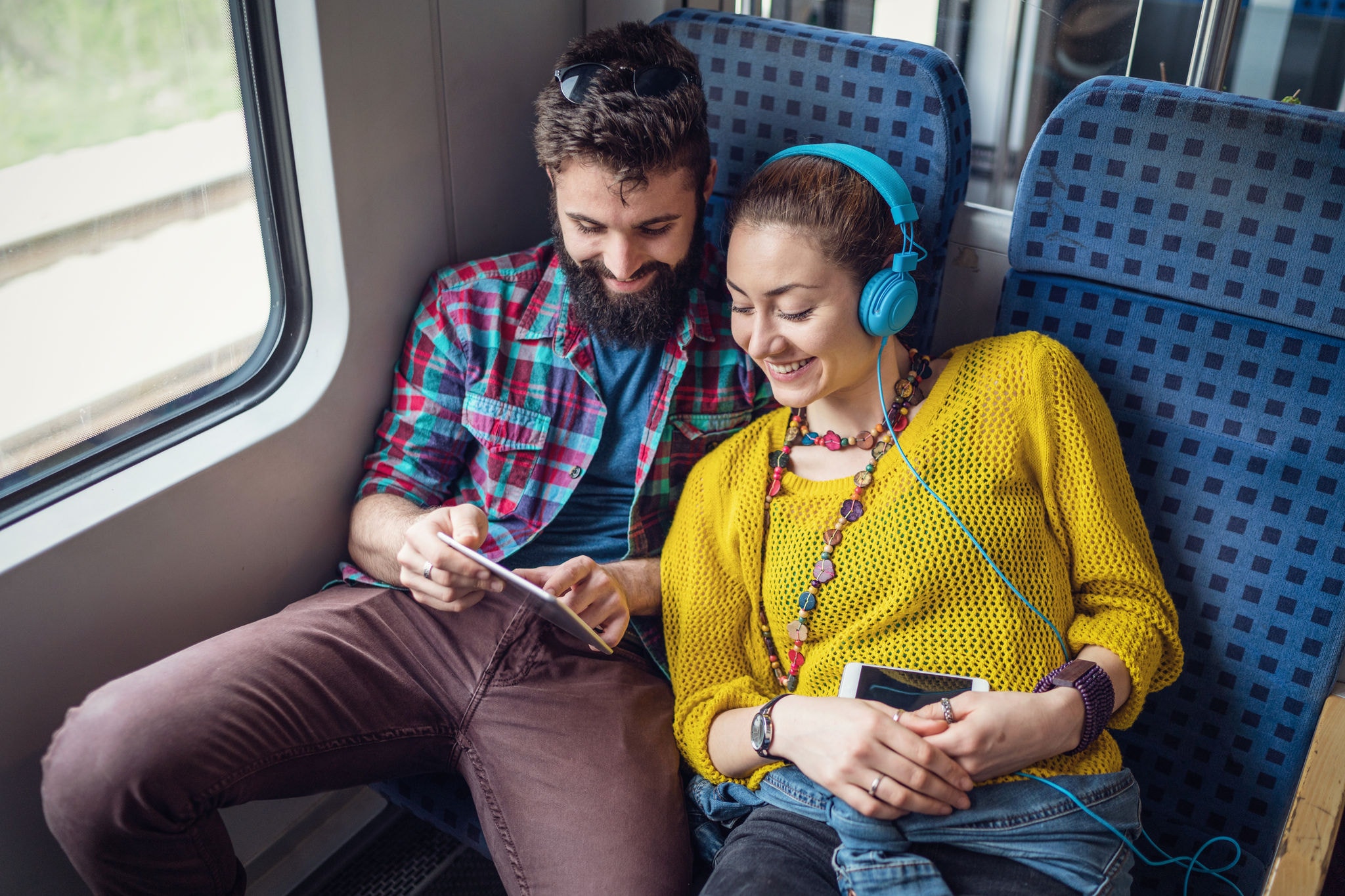 Happy couple listening to music and browsing on the tablet while travelling