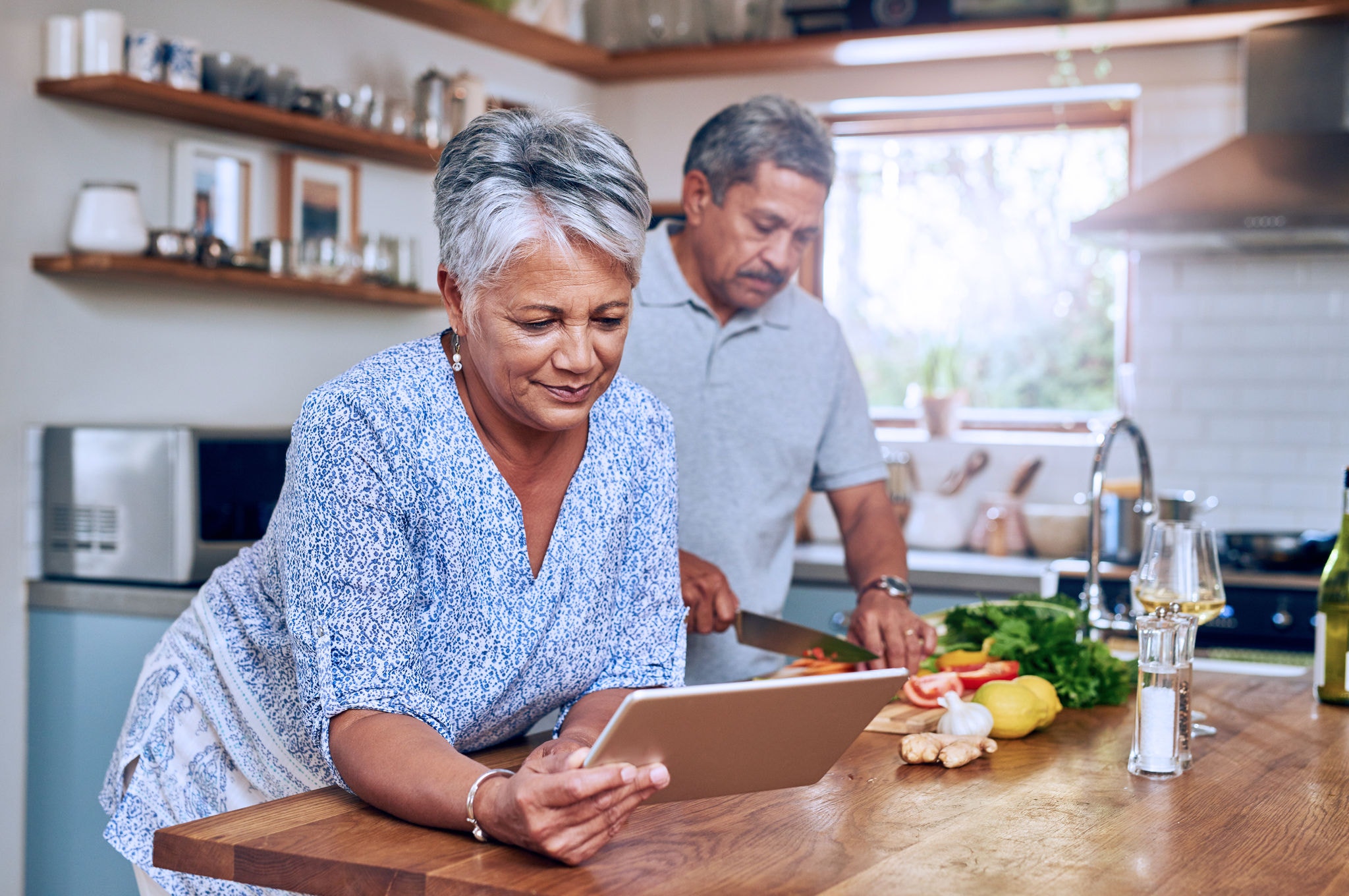 Senior woman and man preparing healthy food together in the kitchen using a tablet