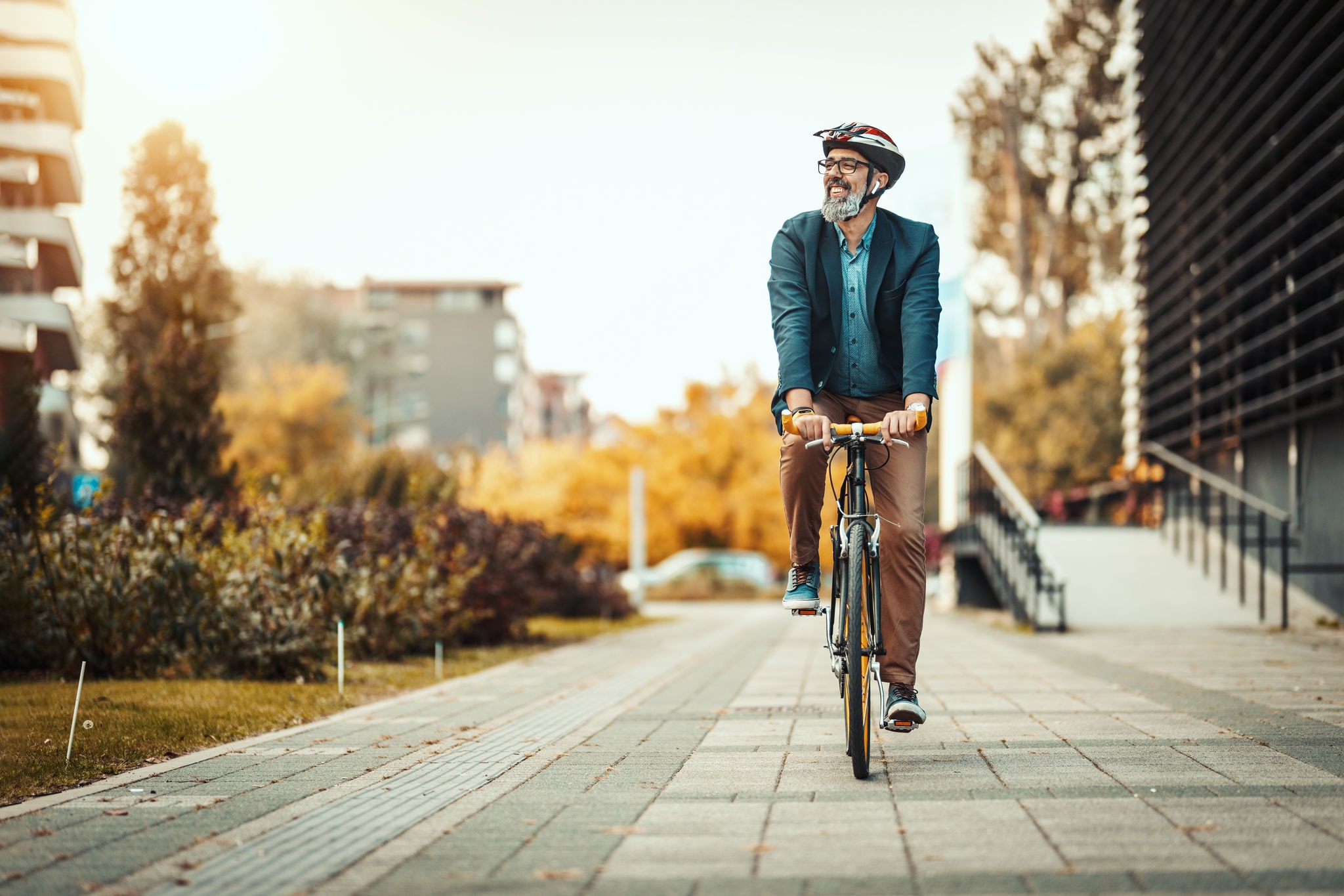 A handsome casual middle-aged businessman is going to the office by bicycle. He is driving bike in front of office district.