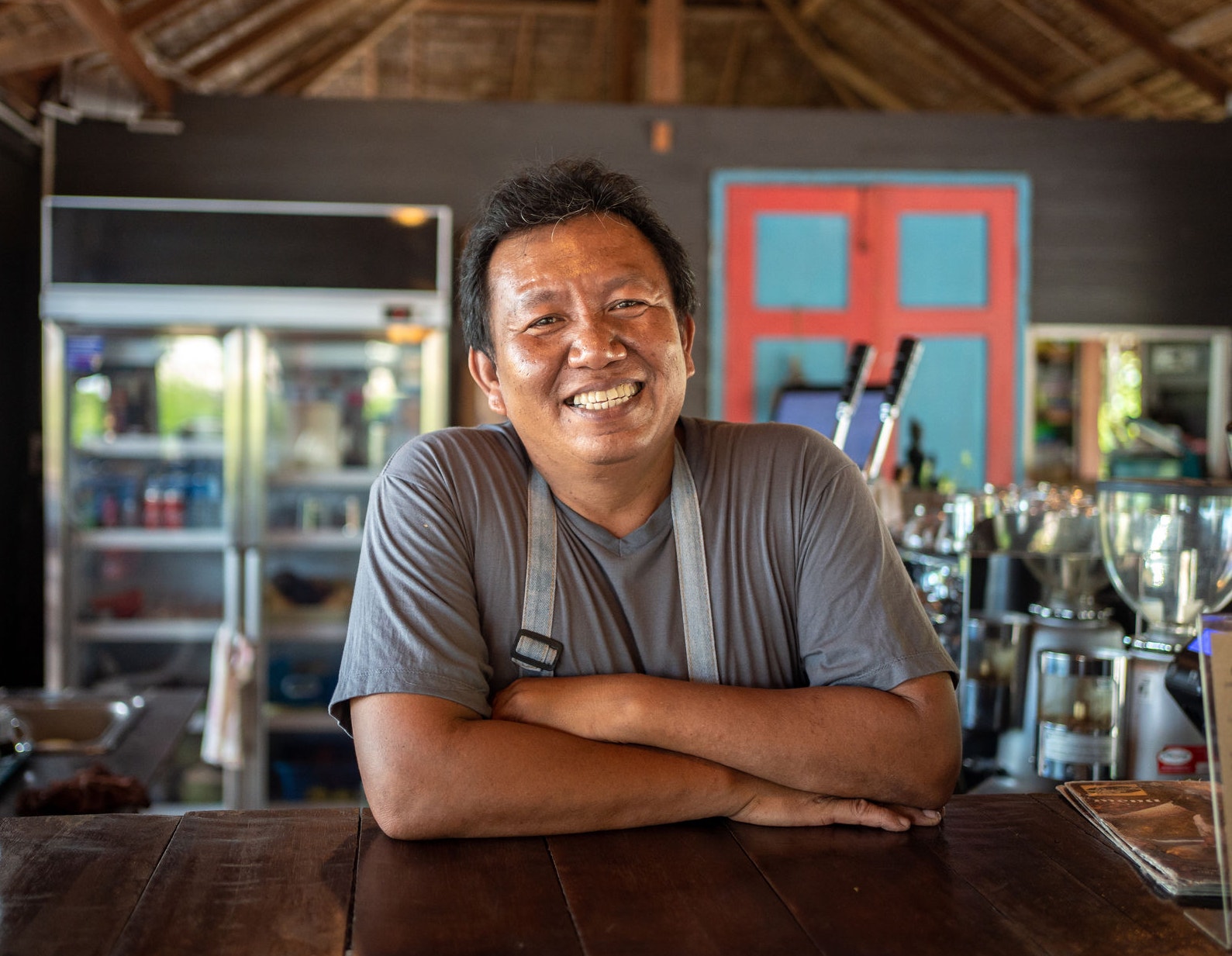 Smiling man is standing at the bar counter and looking at camera in a coffee shop.