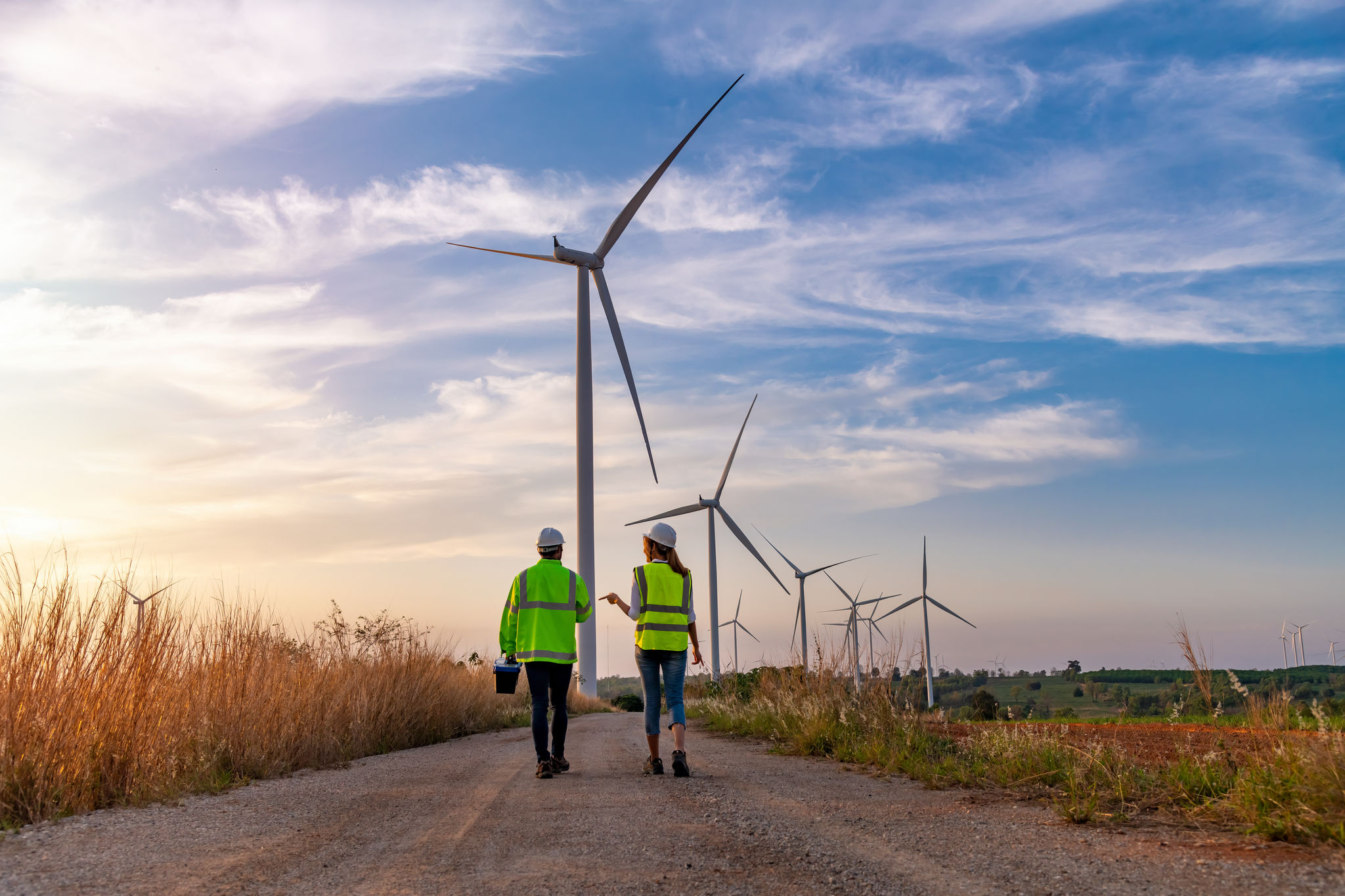Two engineers in uniform inspecting a wind turbine farm for electricity generation