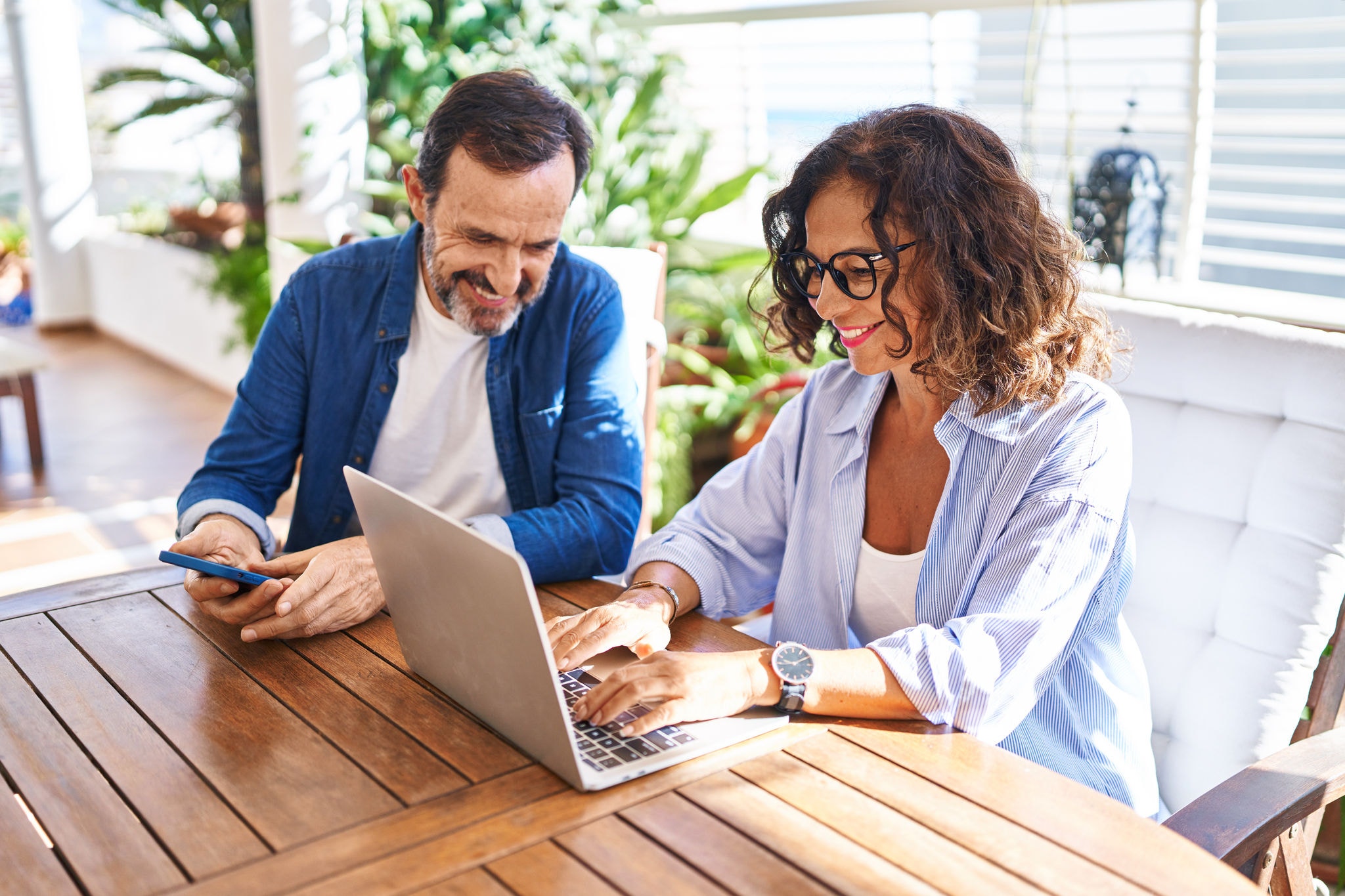 Middle aged couple sitting on their terrace using laptop