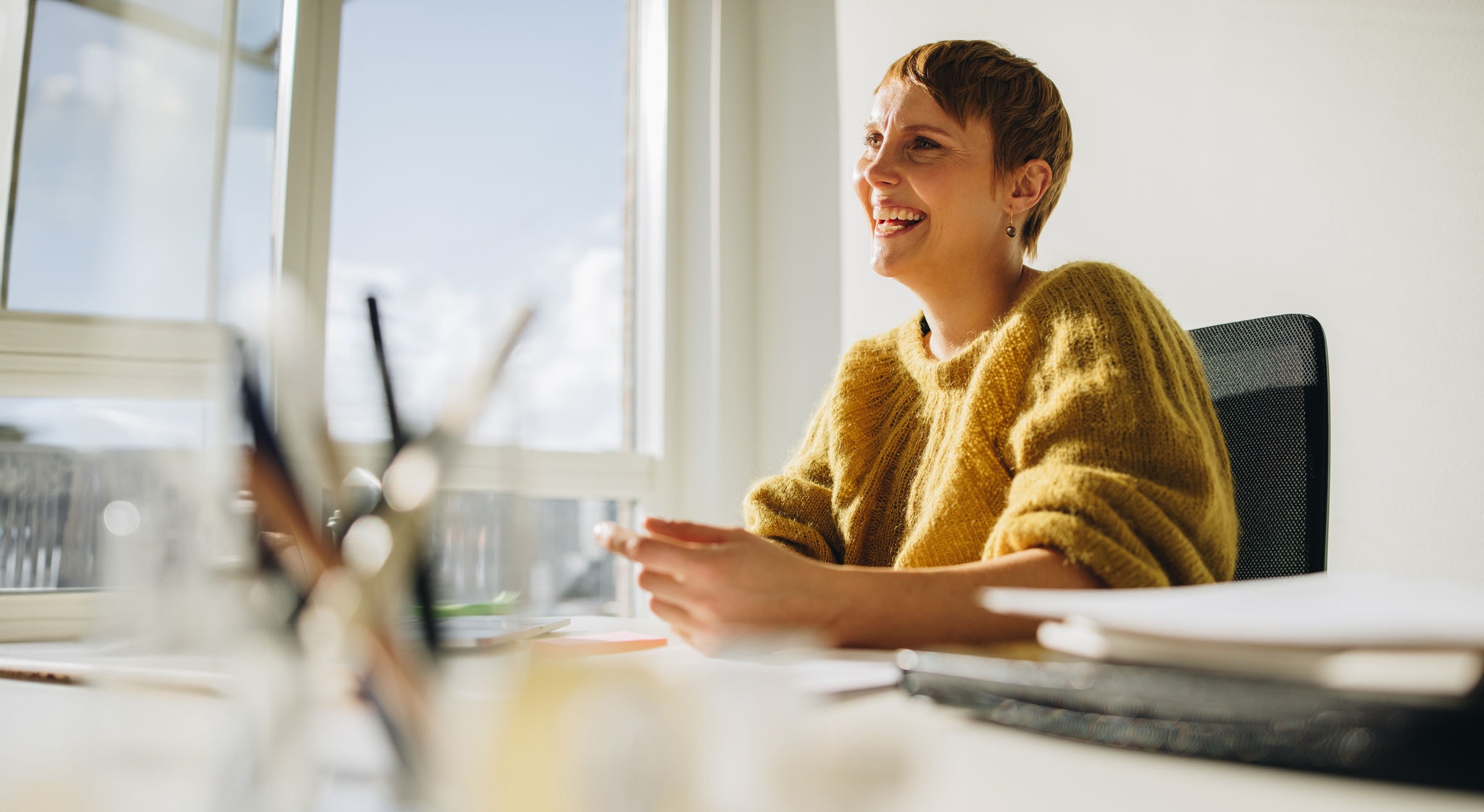 Happy woman executive sitting at desk. Cheerful female sitting at desk and looking away in office.