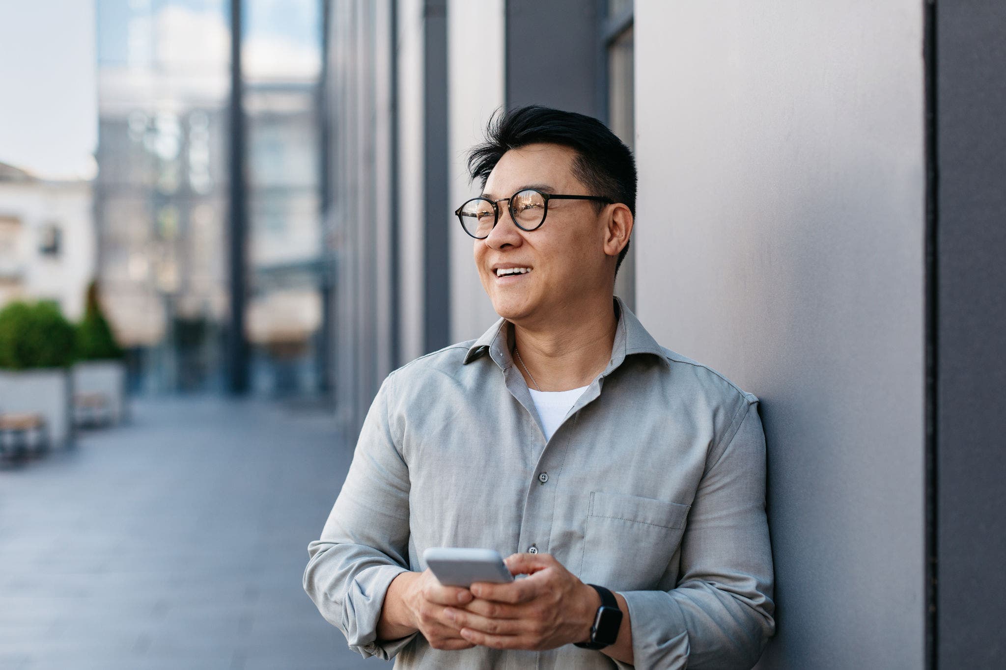 Man standing outdoors, holding a smartphone and looking off into the distance