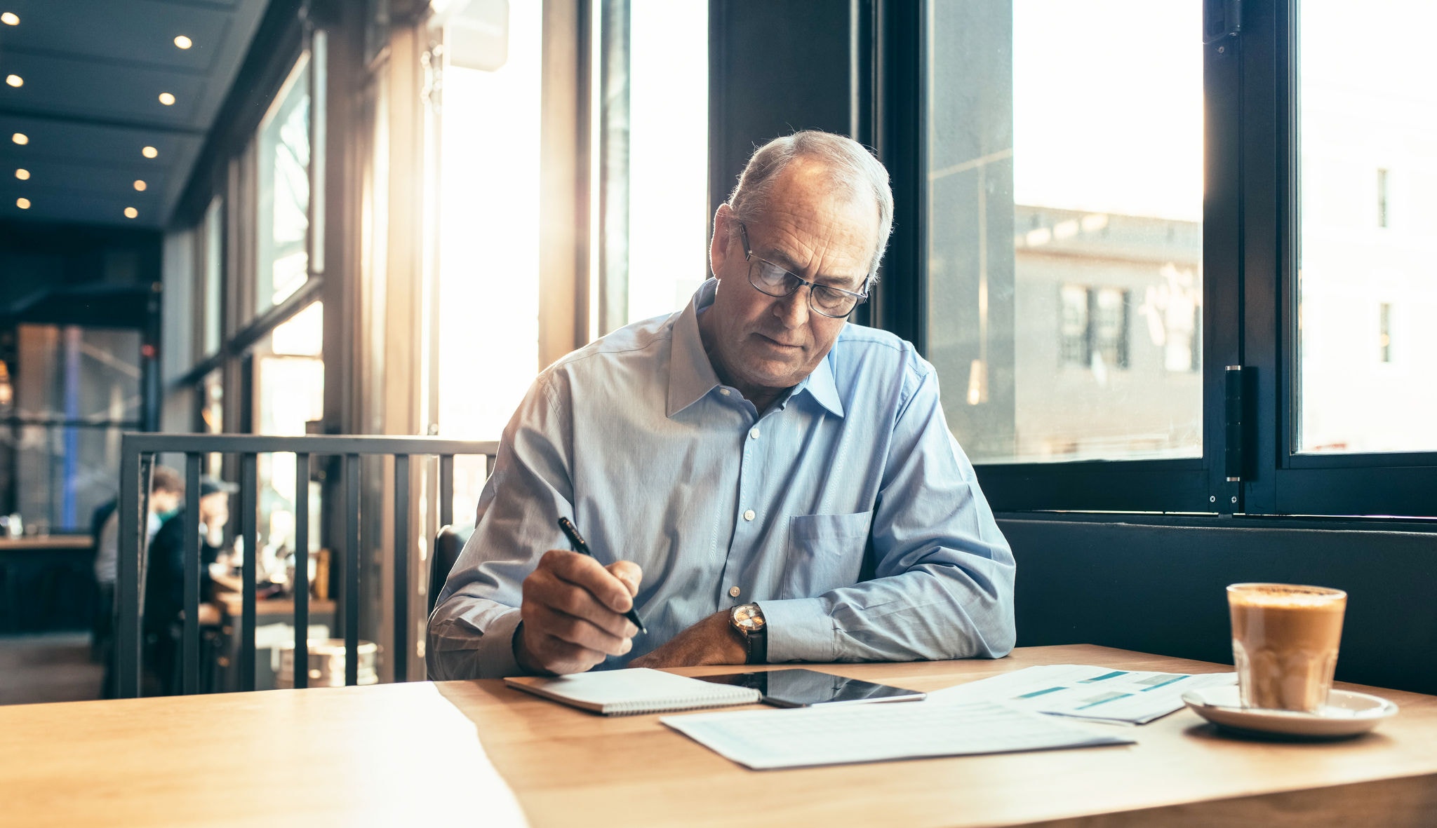 Mature businessman making notes while sitting at cafe. Senior man at modern coffee shop working.
