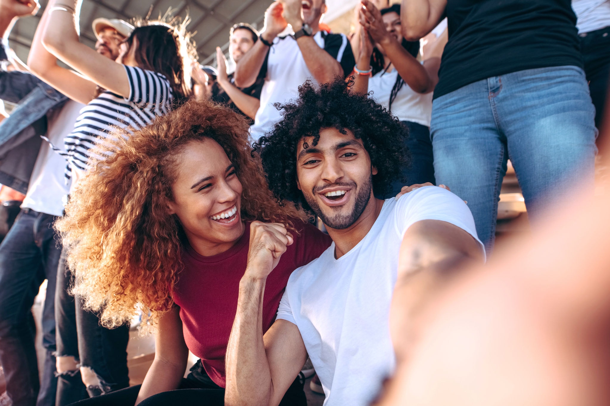 Couple of spectators taking selfie while cheering their sports team from a stadium. Cheerful man and woman fans taking selfie while watching match in stadium.
