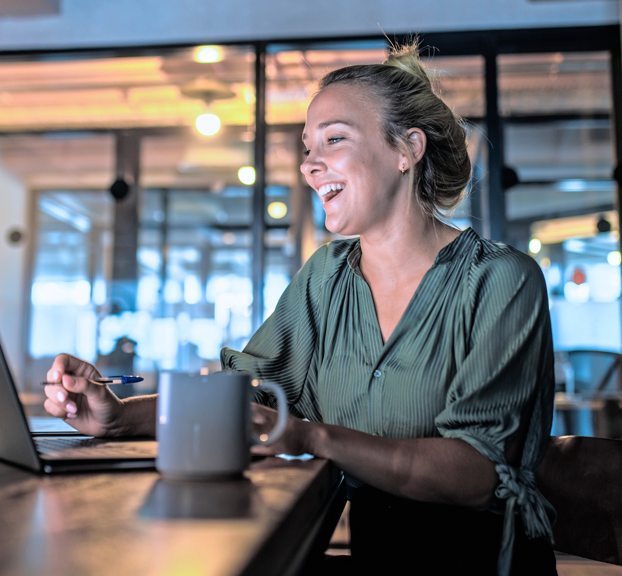 Low angle view of lighthearted Argentine businesswoman in late 20s enjoying video conference on laptop in dimly lit board room.