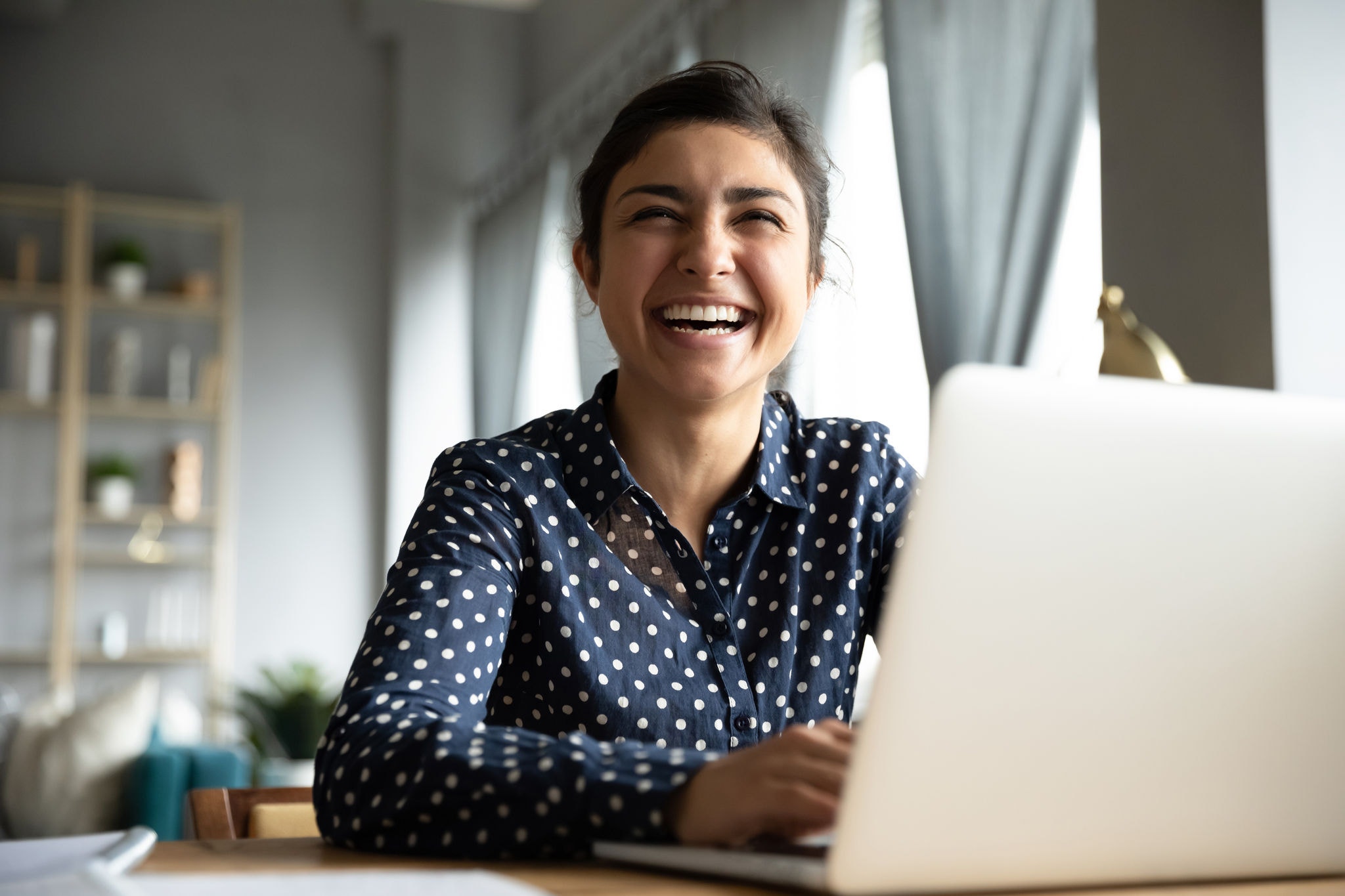 Female student enjoying a moment of laughter while working on her laptop at home