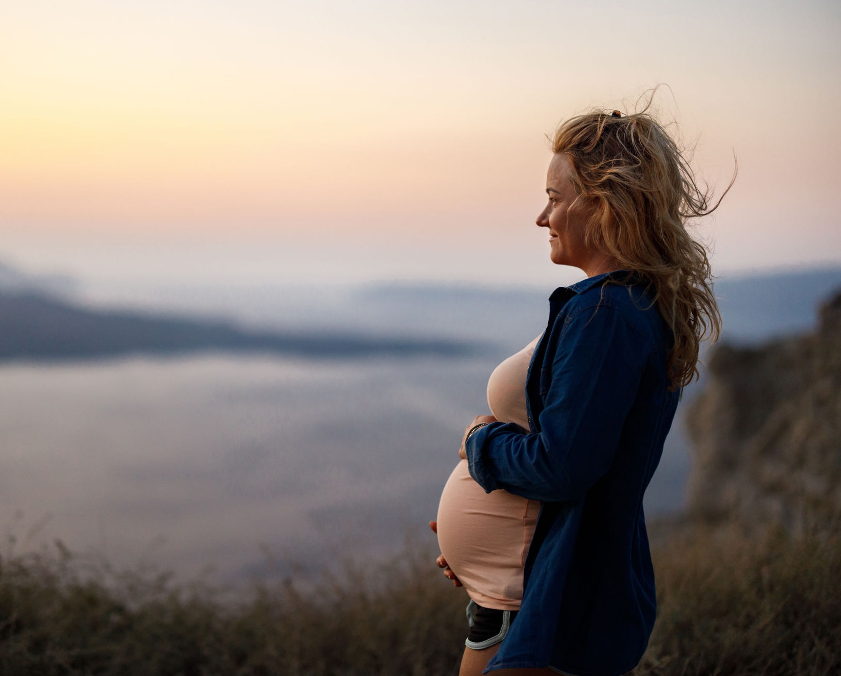 Smiling pregnant woman day dreaming during summer vacation on a hill above the sea