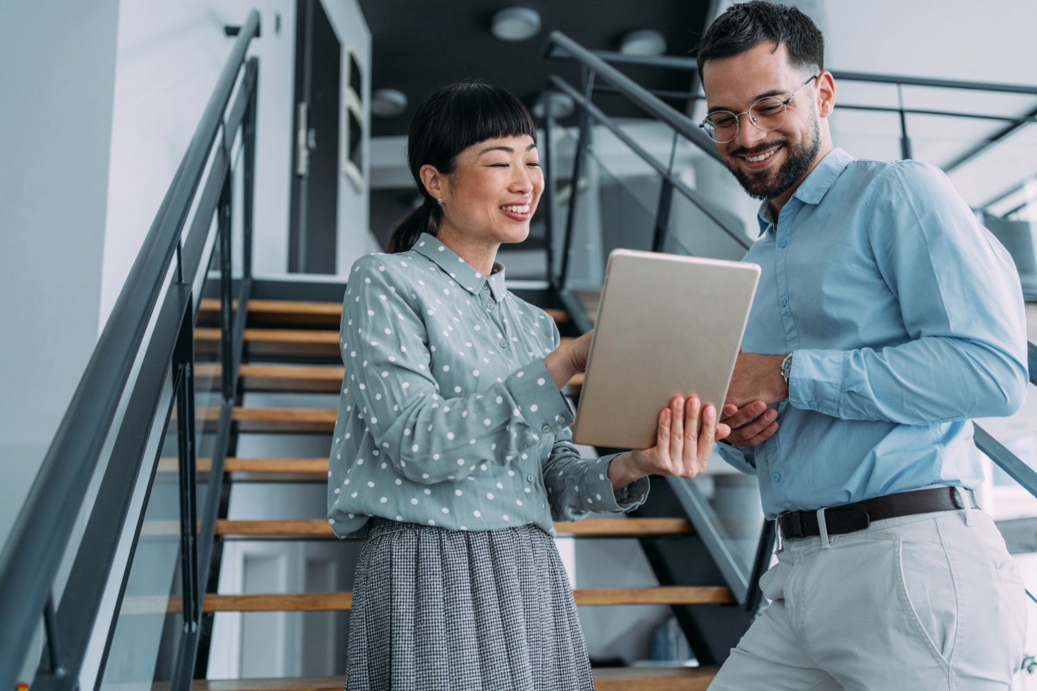 Two colleagues discussing work on a tablet at the bottom of the stairs