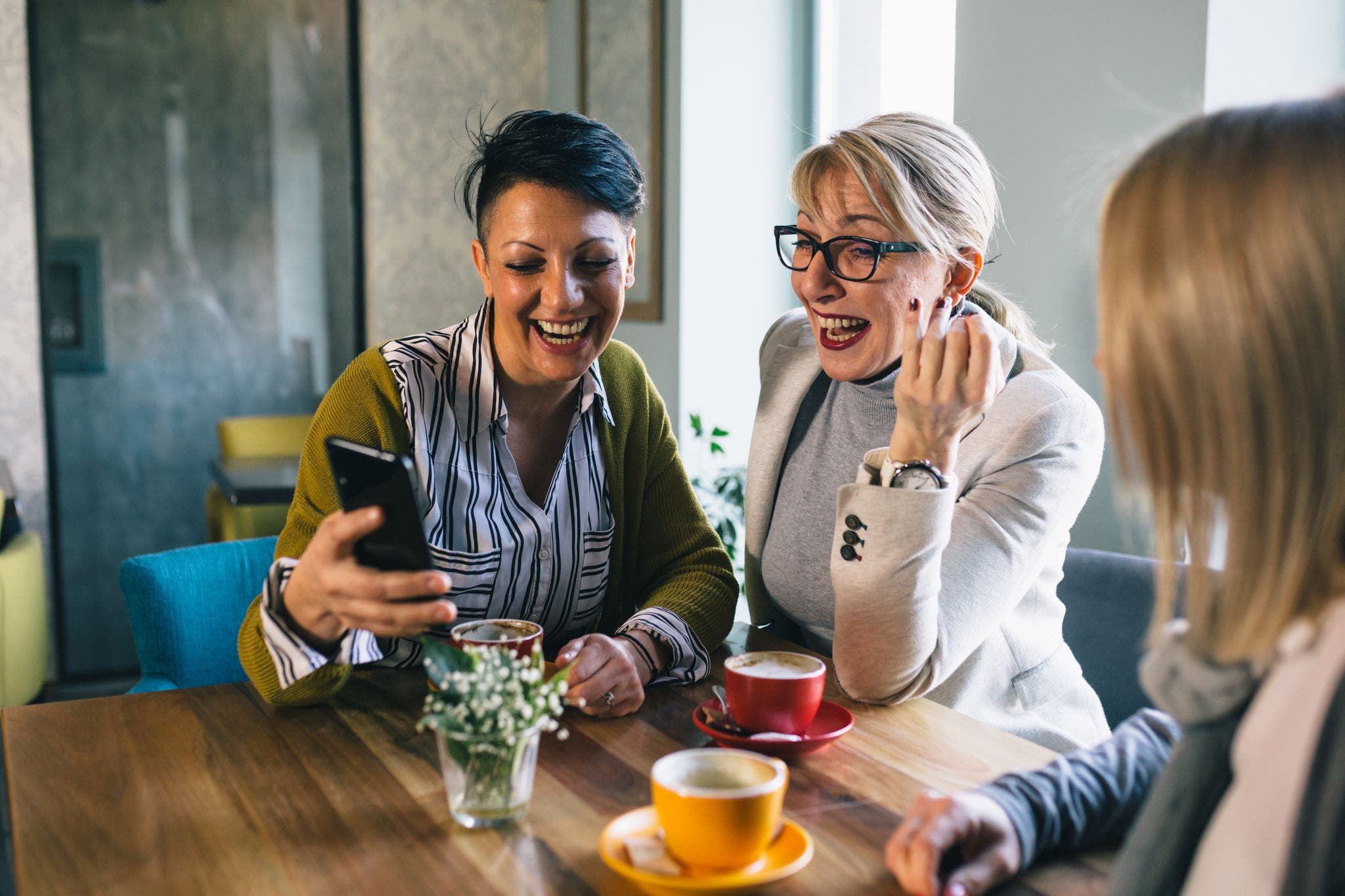mid aged woman friends talking and drinking coffee in cafe, using mobile phone