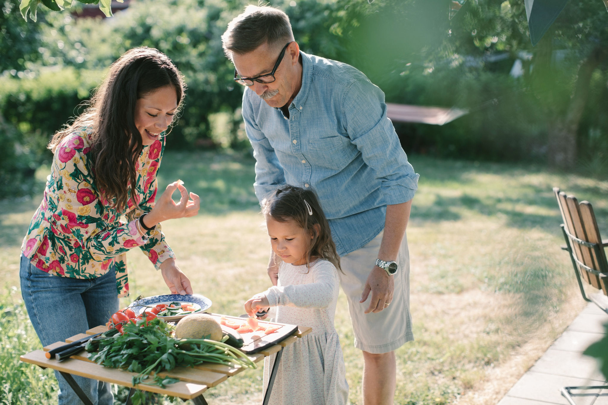 Girl cutting food with mother and grandfather in their backyard