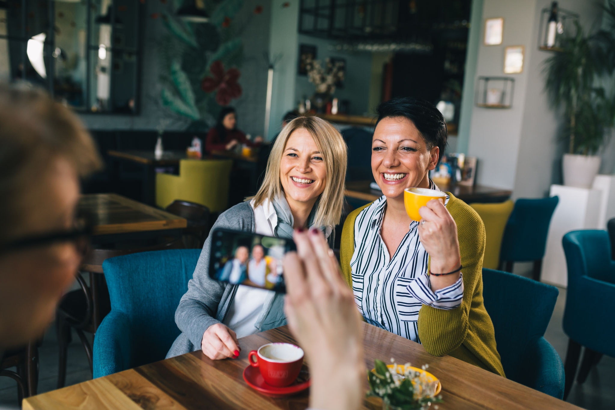 Two female friends pose for a photo while sitting together in a cafe